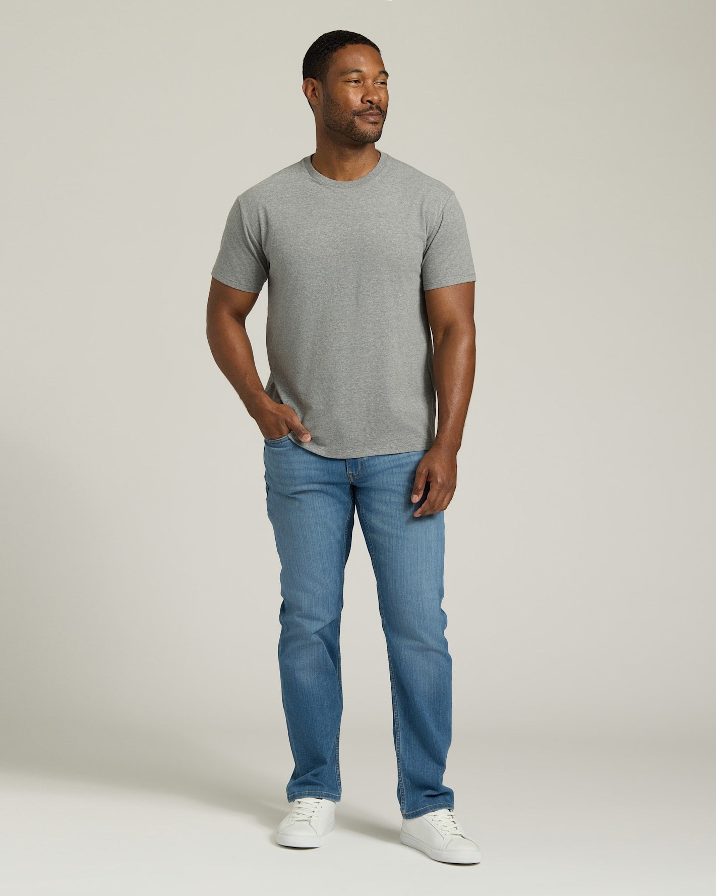 Man wearing a gray t-shirt and blue jeans standing against a plain background. MODEL_INFO: Model is 5'8" wearing size M short