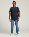 Man wearing a navy t-shirt and blue jeans on a white background. MODEL_INFO: Model is 5'8" wearing size M short