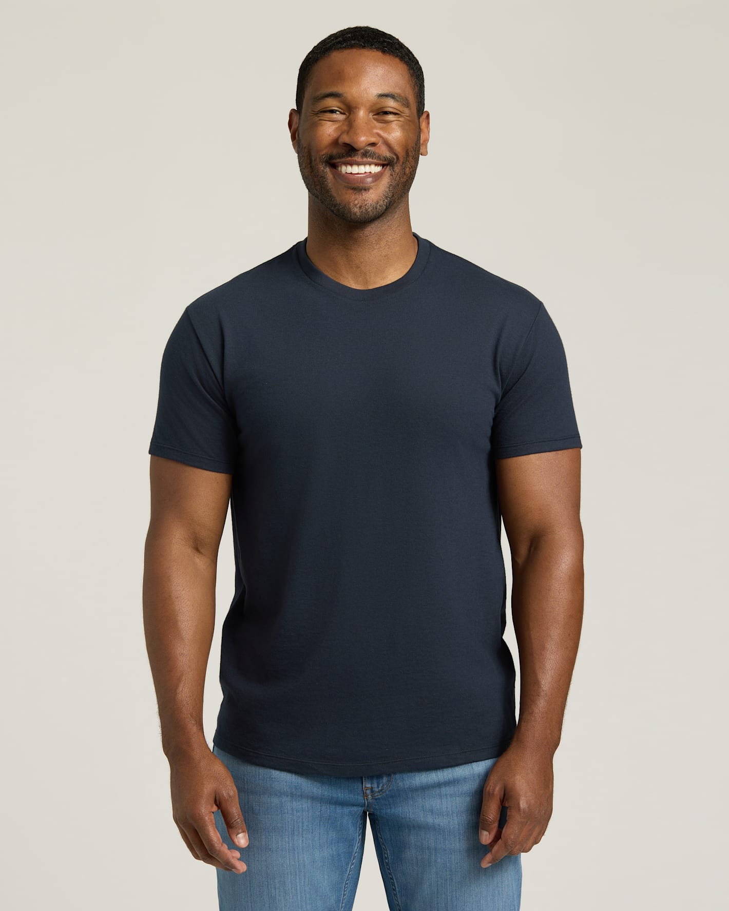 Man wearing a navy blue t-shirt and blue jeans against a plain background. 