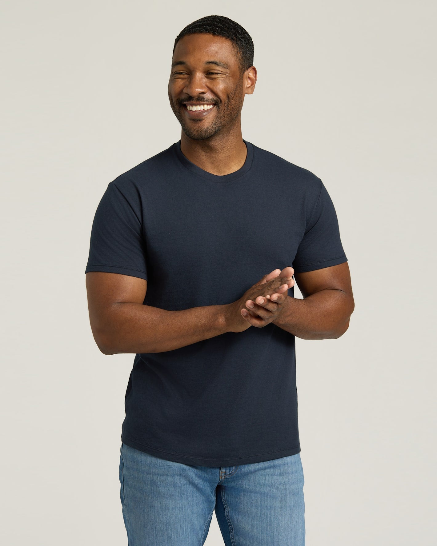 Man wearing a navy blue t-shirt and light blue jeans against a plain background