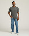 Man wearing a gray t-shirt and blue jeans standing against a plain background. MODEL_INFO: Model is 5'8" wearing size M short