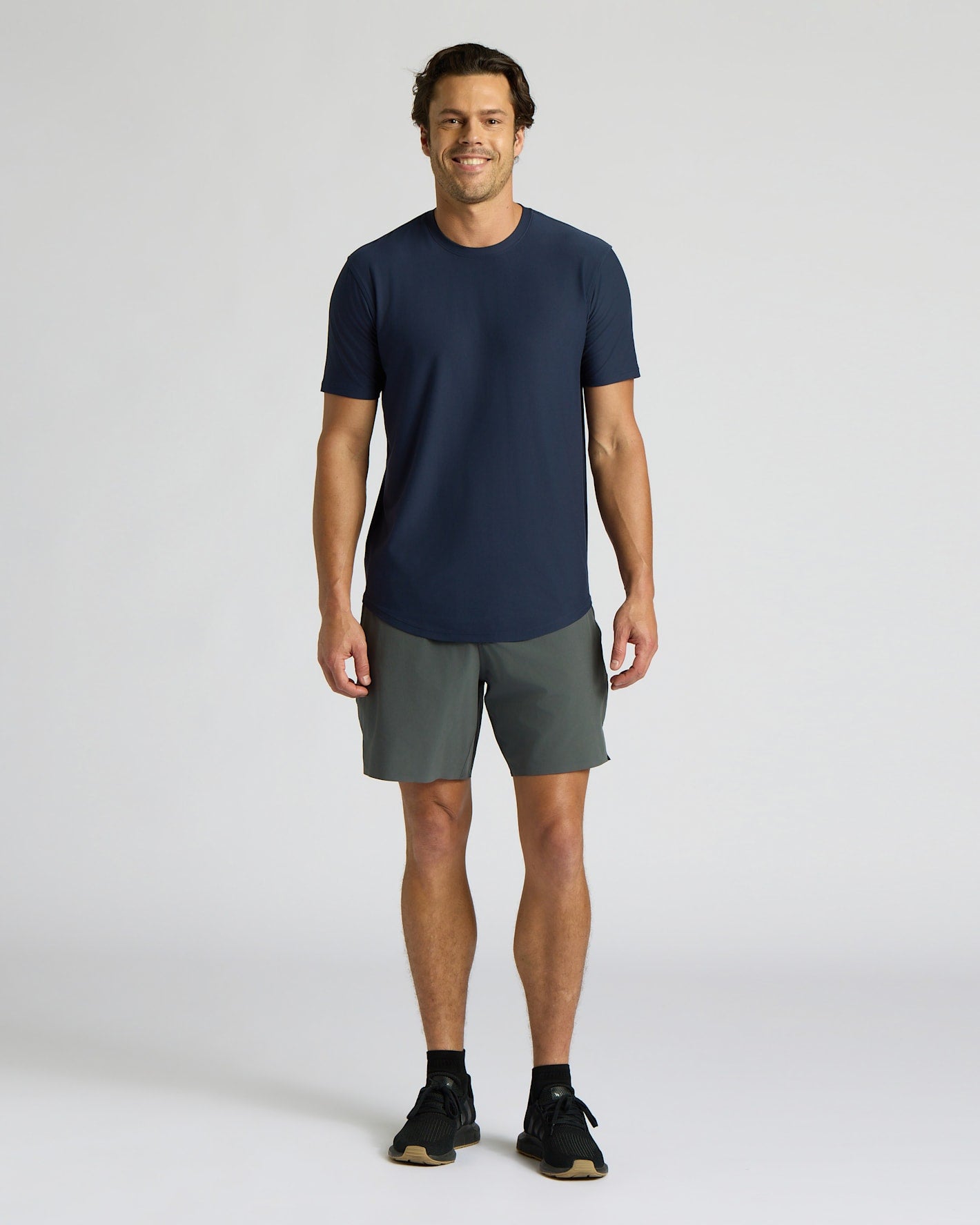 Man wearing a navy t-shirt and gray shorts on a white background