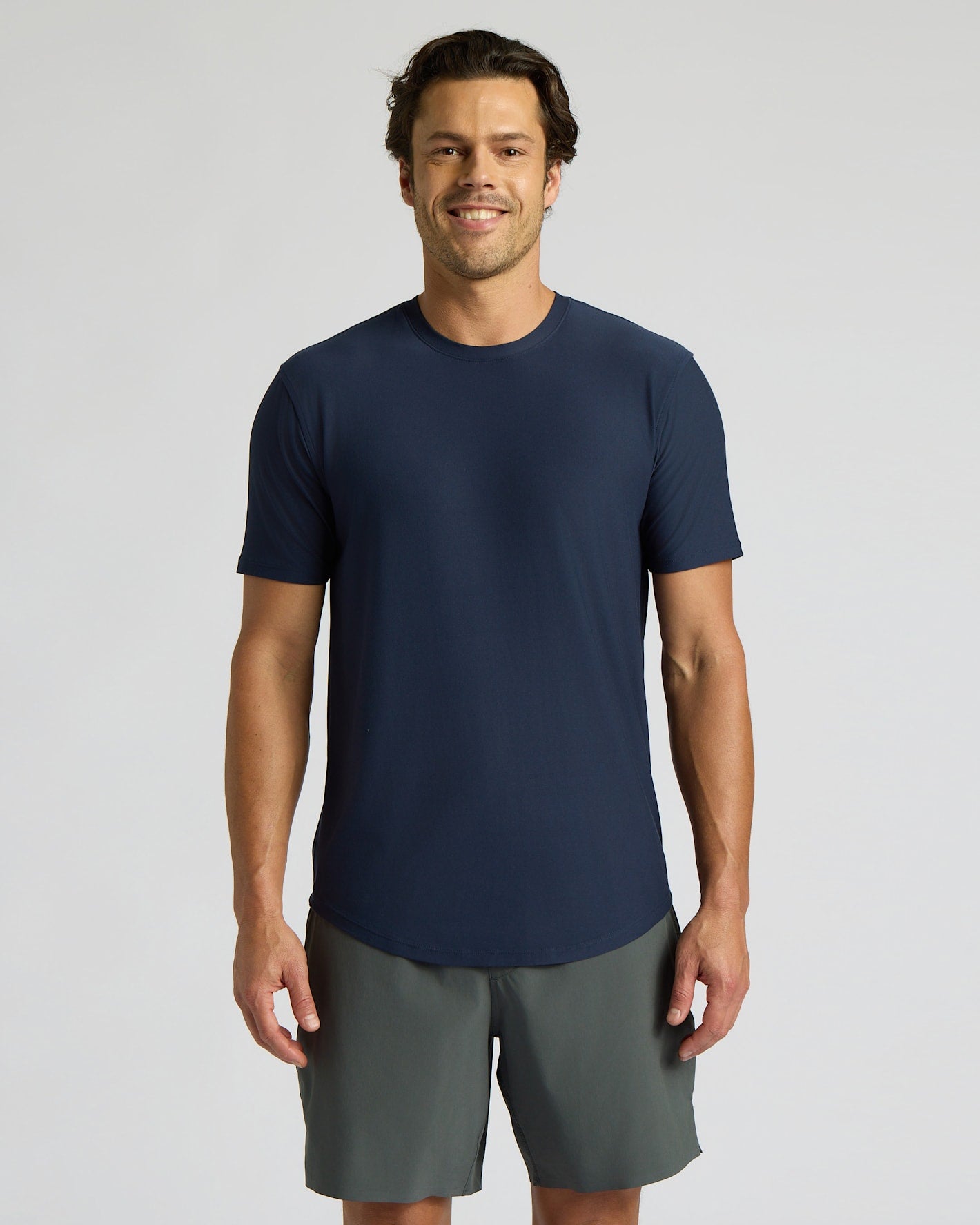 Man wearing a navy blue t-shirt and gray shorts on a light gray background