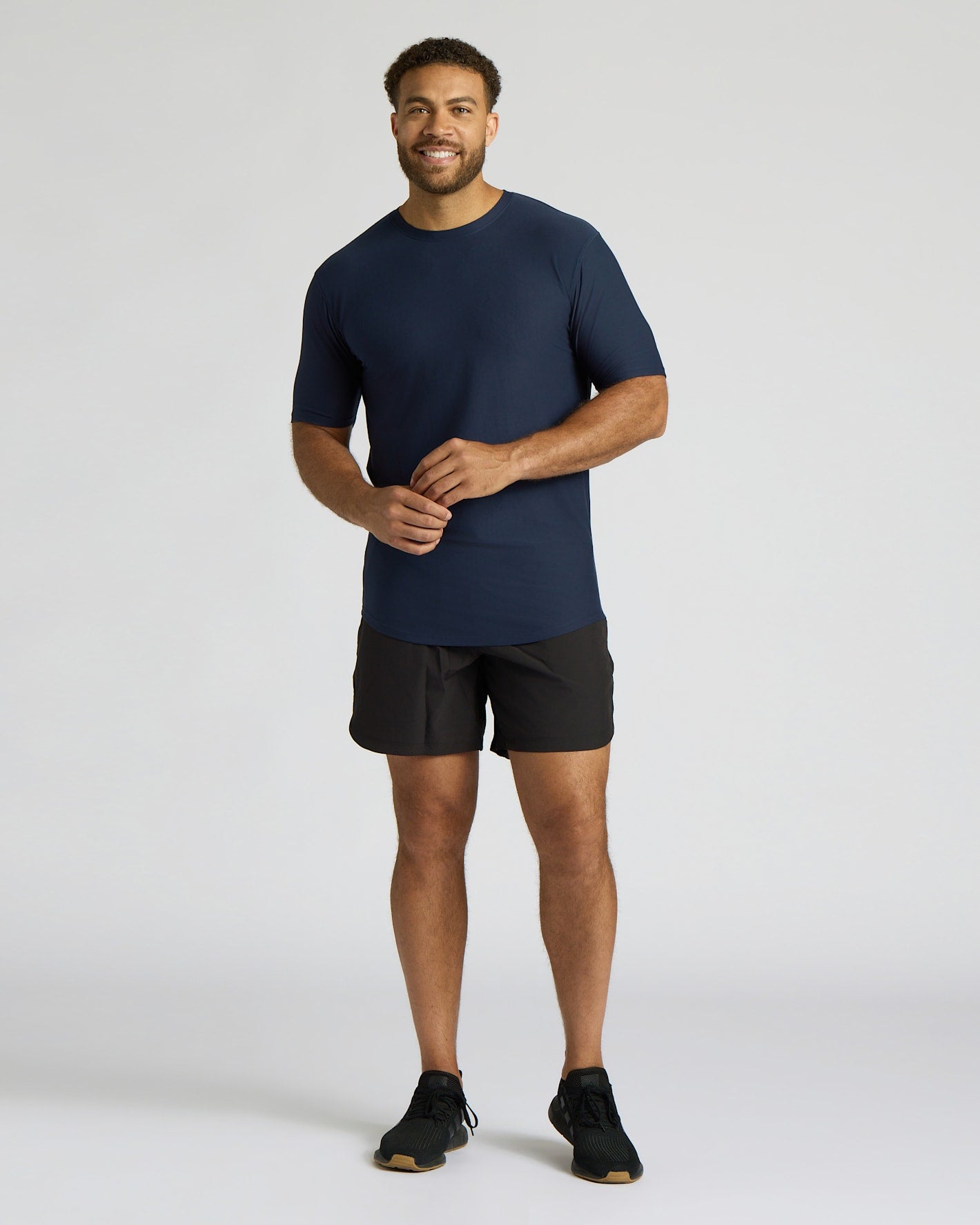 Man wearing a navy t-shirt and black shorts on a light gray background
