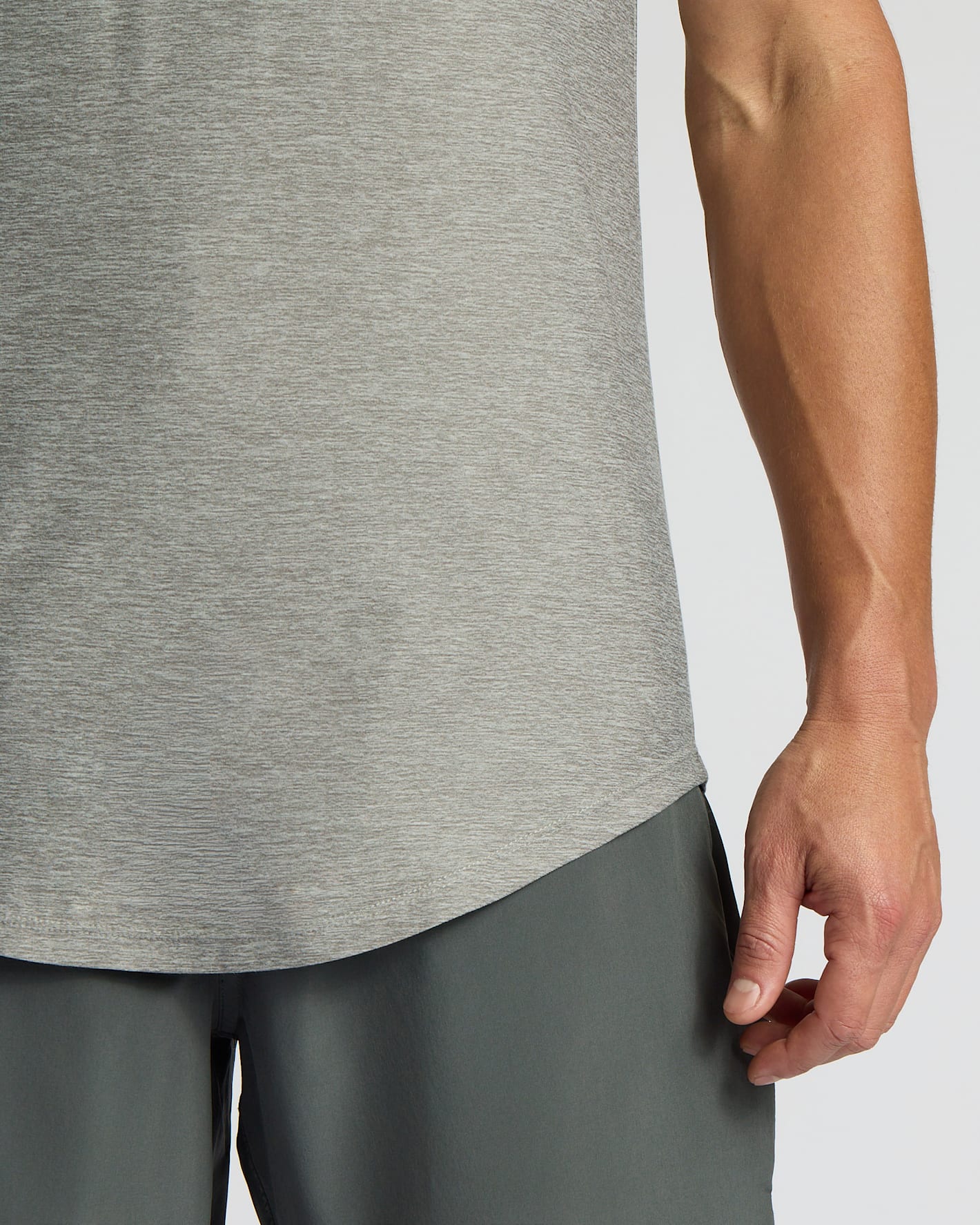 Close-up of a person wearing a heather gray athletic tank top and dark gray athletic shorts against a light gray studio background.
