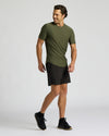 A man modeling an olive green short-sleeve athletic t-shirt and black athletic shorts against a light gray studio background.