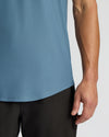 Close-up of a person wearing a muted blue athletic tank top and black shorts against a light gray studio background.