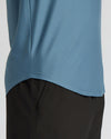 Close-up of a person wearing a dusty blue athletic top and black pants against a light gray background.