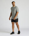 A man modeling a light gray short-sleeve athletic t-shirt and black athletic shorts against a plain light gray studio background.
