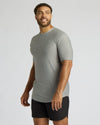 A man wearing a heather gray short-sleeve athletic t-shirt and black athletic shorts, standing against a light gray studio background.