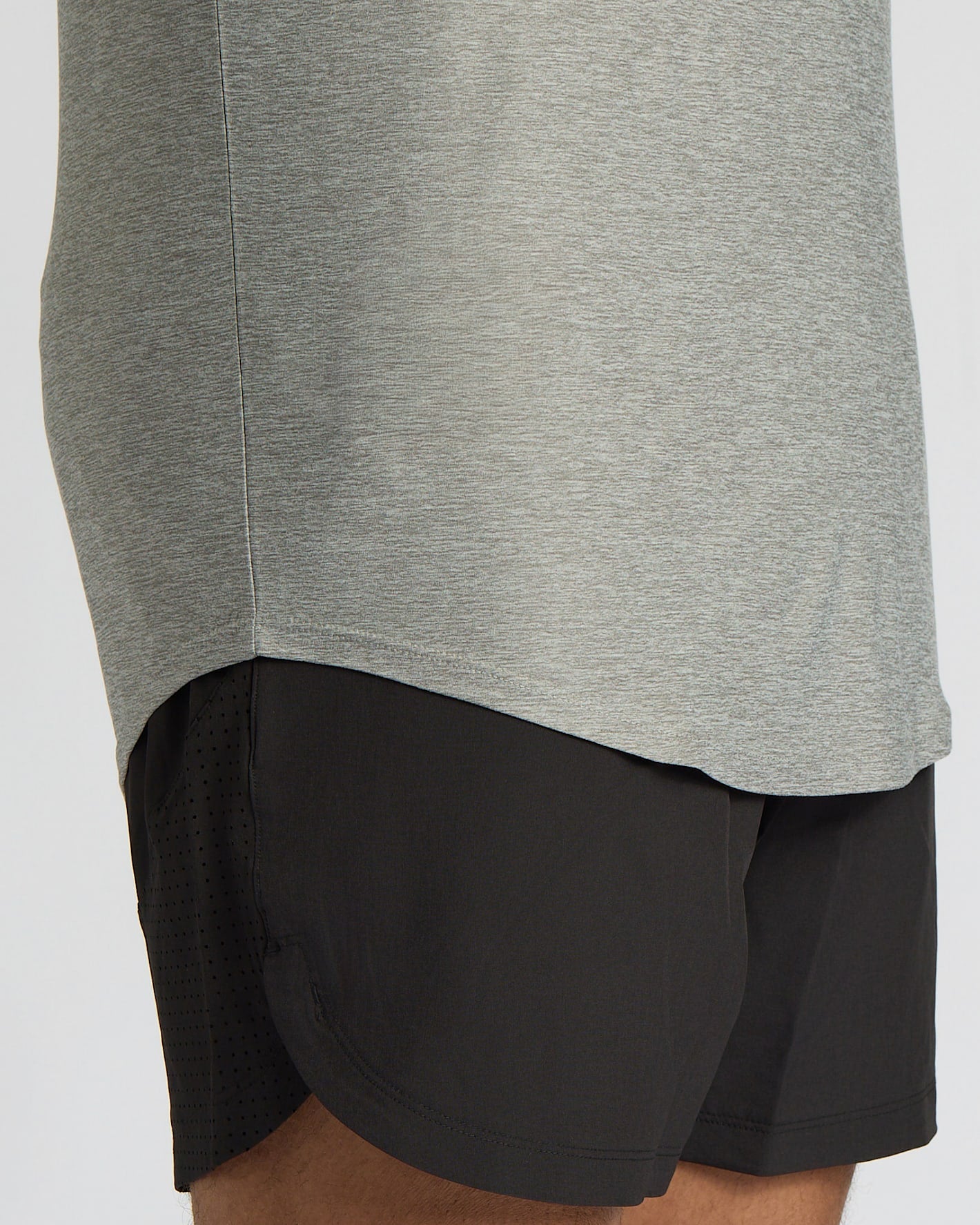 Close-up of a person wearing a heather gray athletic top and black athletic shorts against a light gray background.