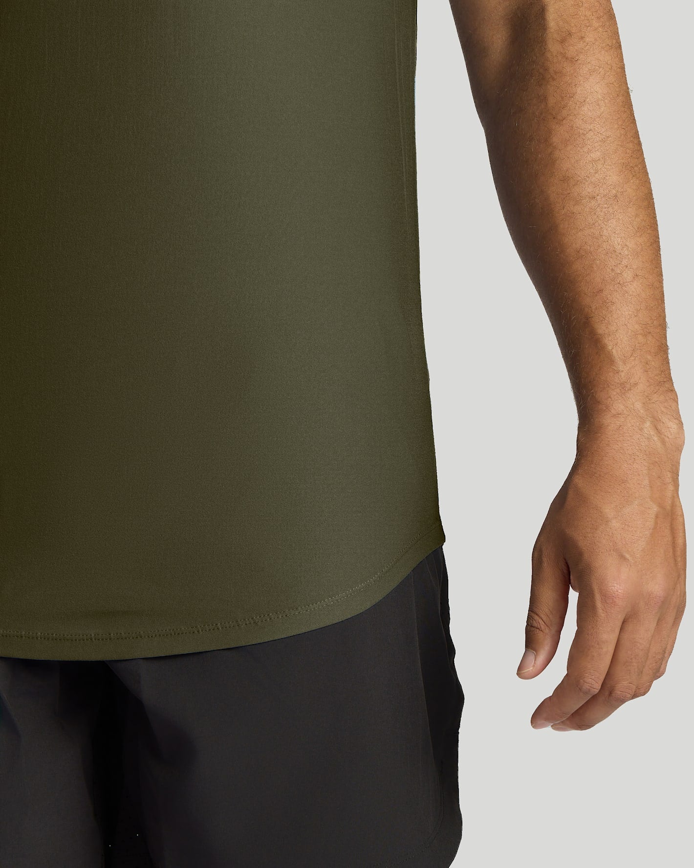 Close-up of a person wearing an olive green athletic top and dark shorts against a light gray background.