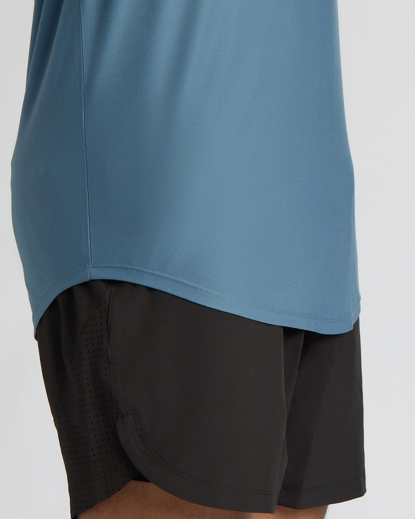 Close-up of a person wearing a dusty blue athletic top and black athletic shorts against a light gray studio background.