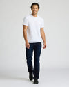 Man wearing a white t-shirt and dark jeans on a plain background. MODEL_INFO: Model is 6'0" wearing size L short