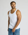 Man wearing a white tank top and blue jeans against a plain background