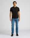 Man wearing a black t-shirt and blue jeans on a white background. MODEL_INFO: Model is 6'0" wearing size L short