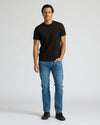 Man wearing a black t-shirt and blue jeans on a white background. MODEL_INFO: Model is 6'0" wearing size L short
