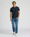 Man wearing a navy t-shirt and blue jeans on a white background. MODEL_INFO: Model is 6'0" wearing size L short