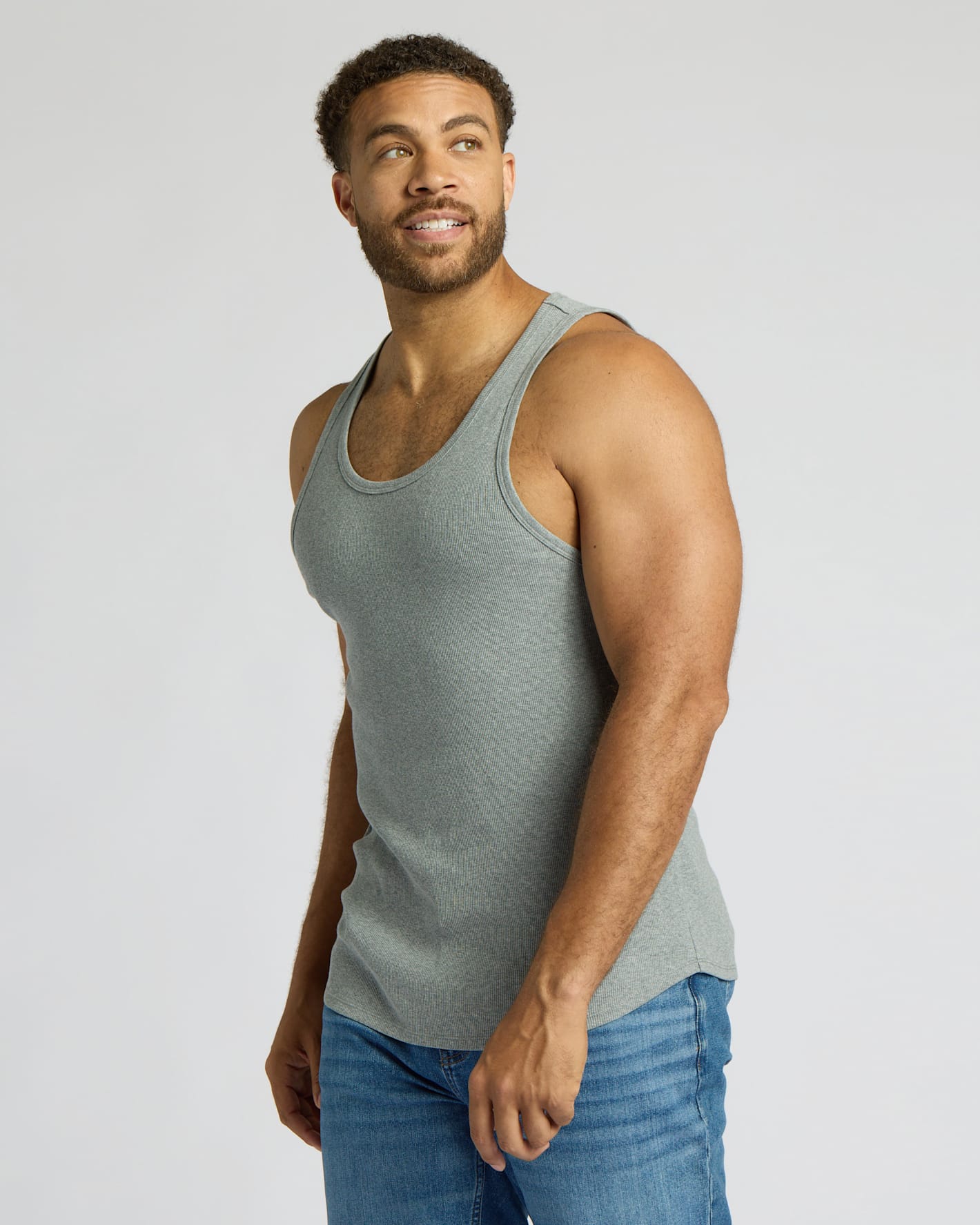 Man wearing a green tank top and blue jeans on a light gray background