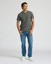 Man wearing a gray t-shirt and blue jeans on a white background. MODEL_INFO: Model is 6'0" wearing size L short
