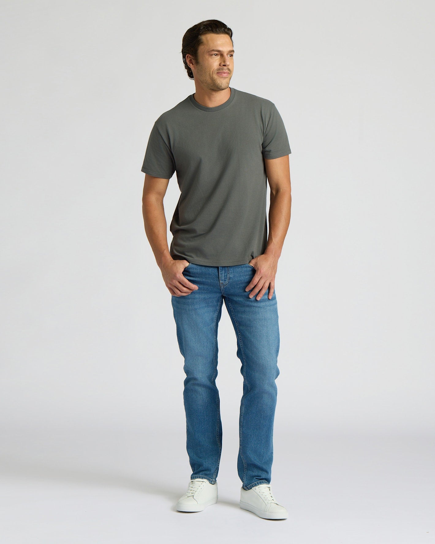 Man wearing a gray t-shirt and blue jeans on a white background. MODEL_INFO: Model is 6'0" wearing size L short