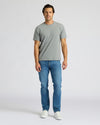 Man wearing a gray t-shirt and blue jeans on a white background. MODEL_INFO: Model is 6'0" wearing size L short