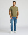 Man wearing an olive green t-shirt and blue jeans on a white background. MODEL_INFO: Model is 6'0" wearing size L short