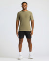 Man wearing an olive green t-shirt and black shorts on a white background