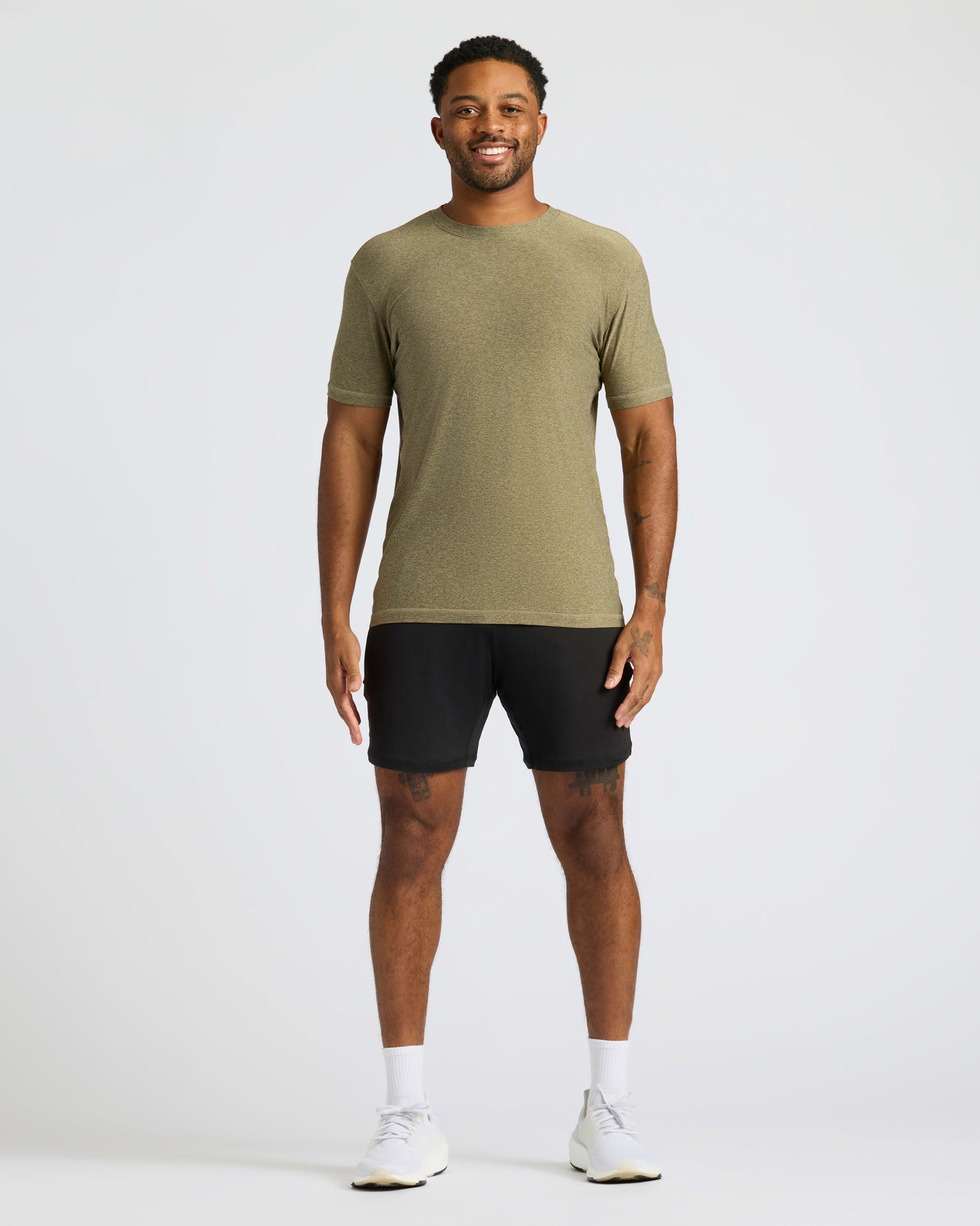 Man wearing an olive green t-shirt and black shorts on a white background