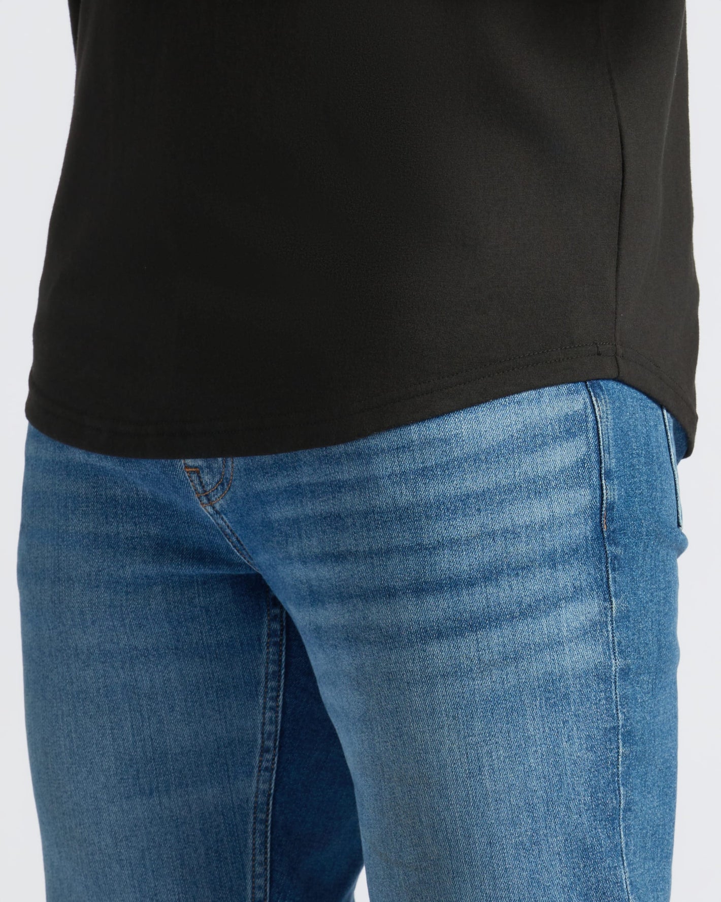 Person wearing All Black Curved Hem Classic Crew Neck, medium-blue jeans visible.