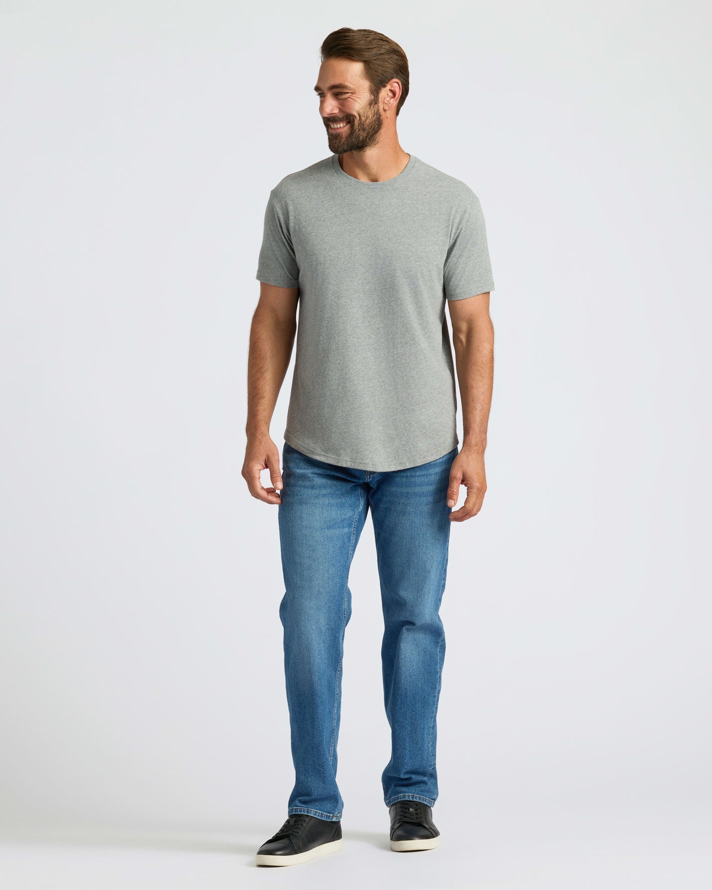Man wearing Heather Gray Curved Hem Classic Crew Neck, blue jeans, and black sneakers.
