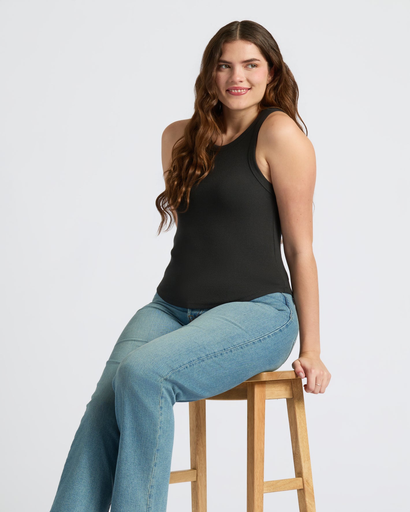 Woman wearing Womens Black Ribbed High Neck Tank 3-Pack, smiling on stool.