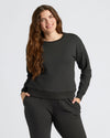 Woman in Womens Black Slouch Pullover Crew, smiling, hands in pockets.