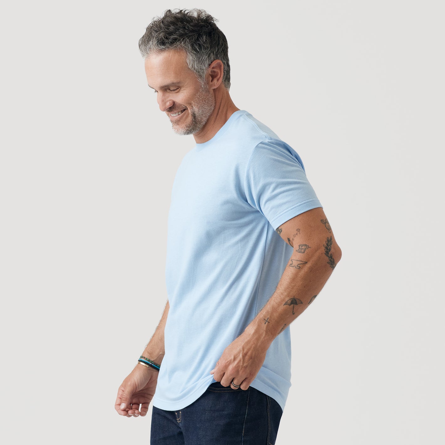 Man in Oxford Blue Short Sleeve Crew Neck Tee, dark jeans, smiling.
