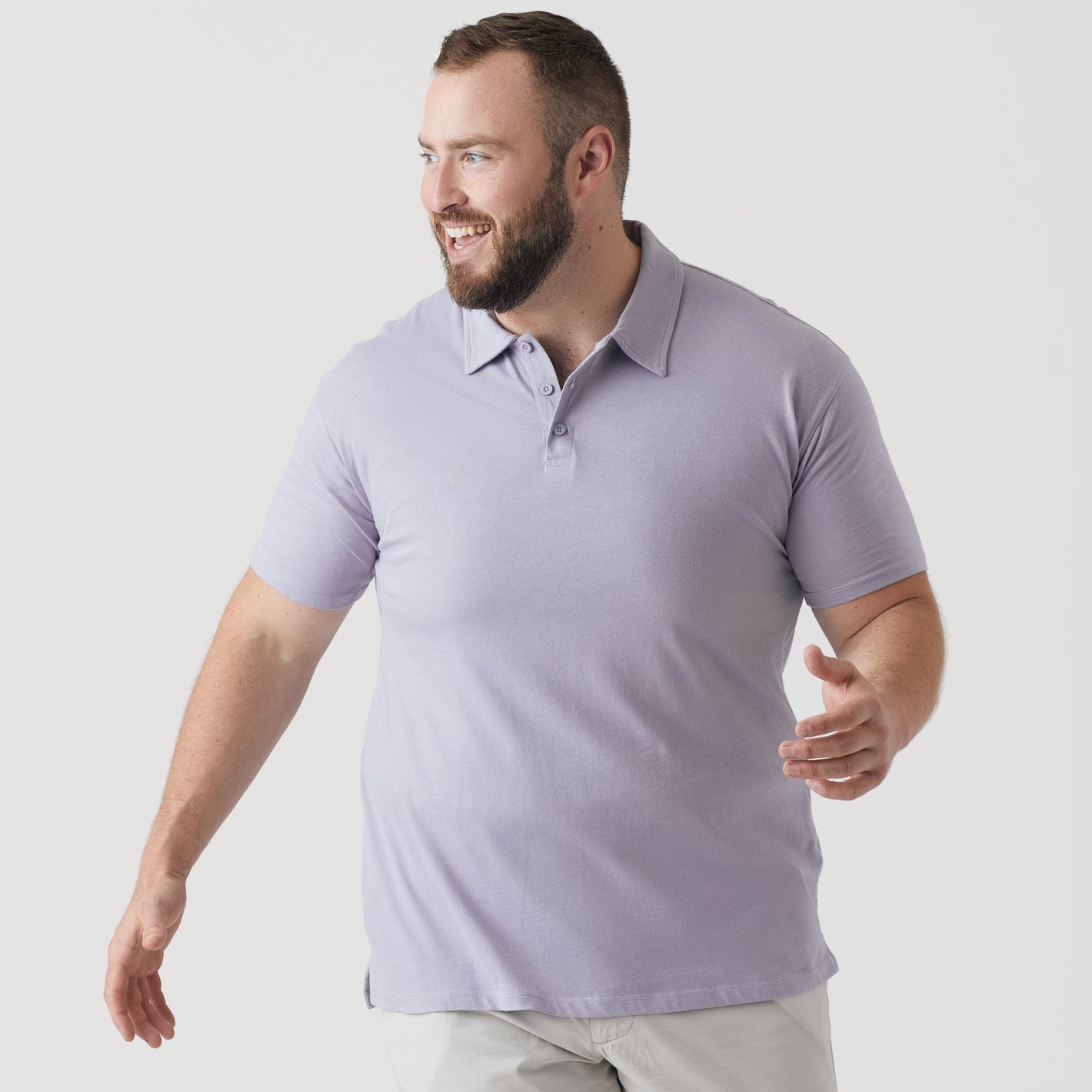 Man wearing Lilac Gray Short Sleeve Polo, smiling, in mid-step against neutral background.