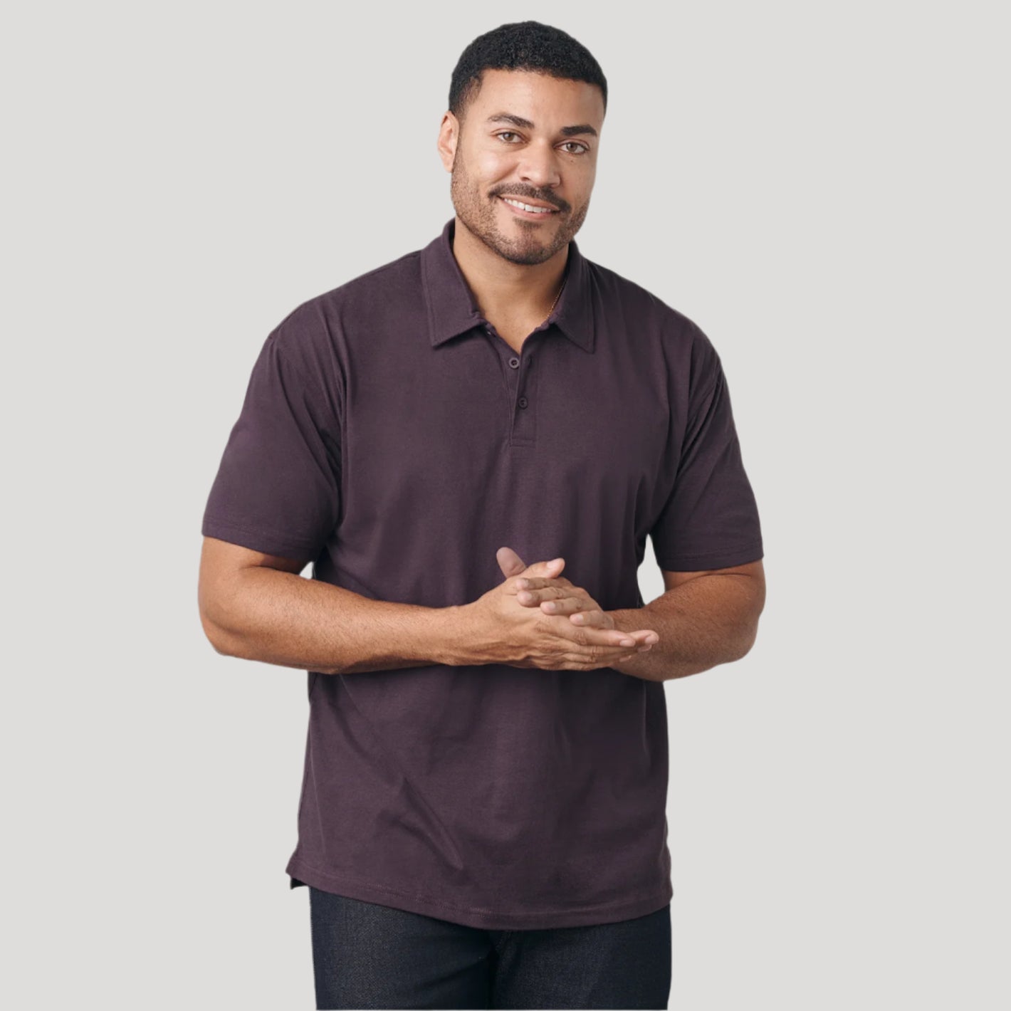 Man wearing Dark Purple Short Sleeve Polo, smiling, hands clasped.