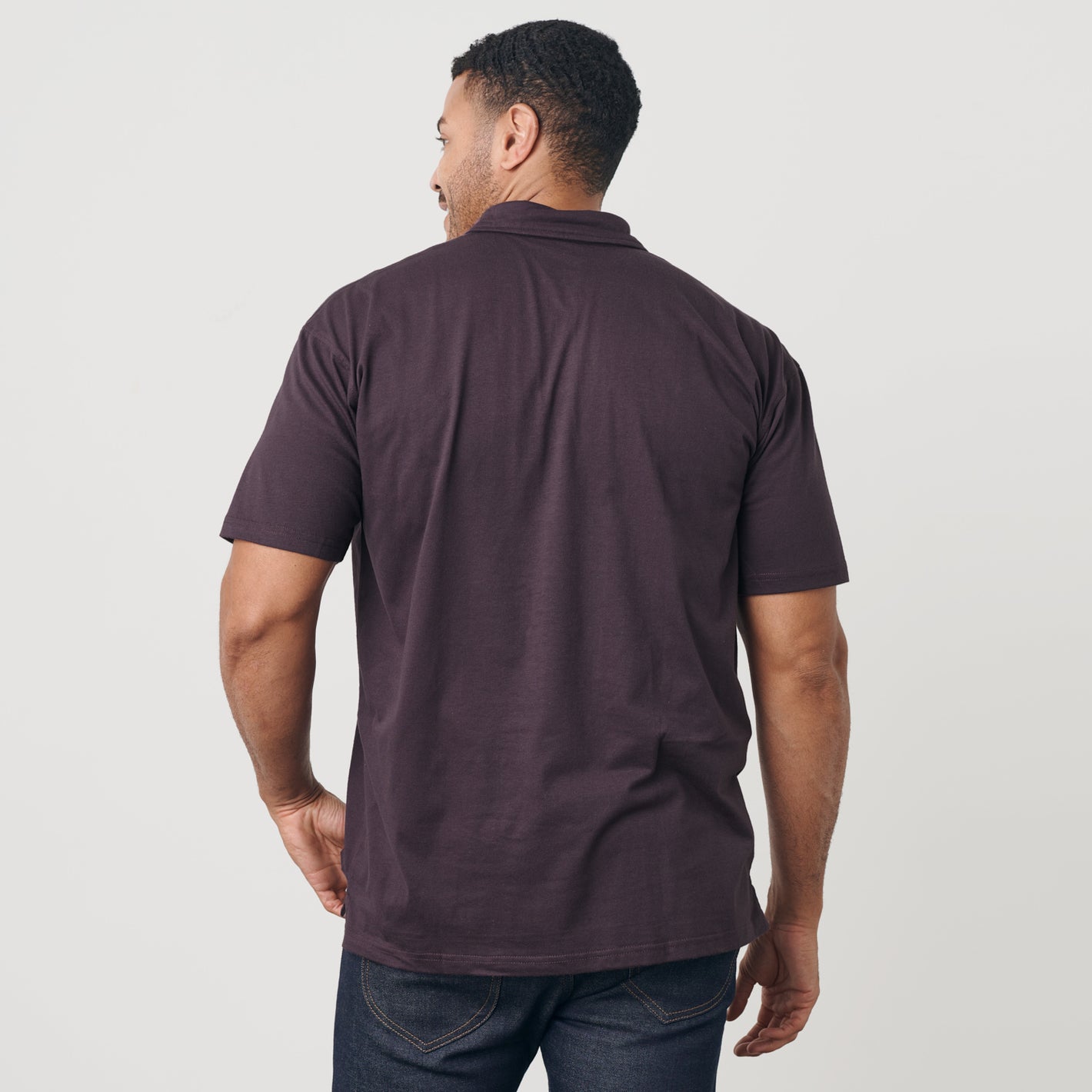 Man wearing Dark Purple Short Sleeve Polo with blue jeans, rear view.