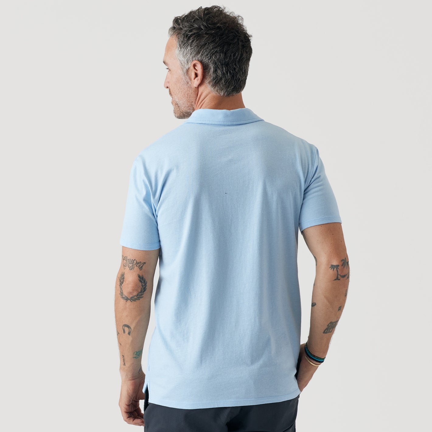 Man wearing Oxford Blue Short Sleeve Polo, showcasing tattooed arms and bracelets.