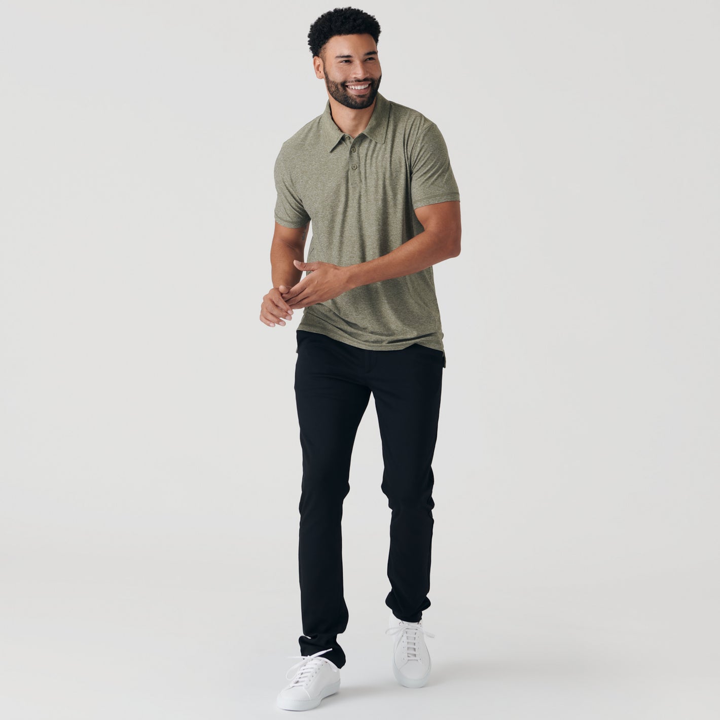 Man wearing Heather Military Green Active Short Sleeve Polo, black trousers, white sneakers.