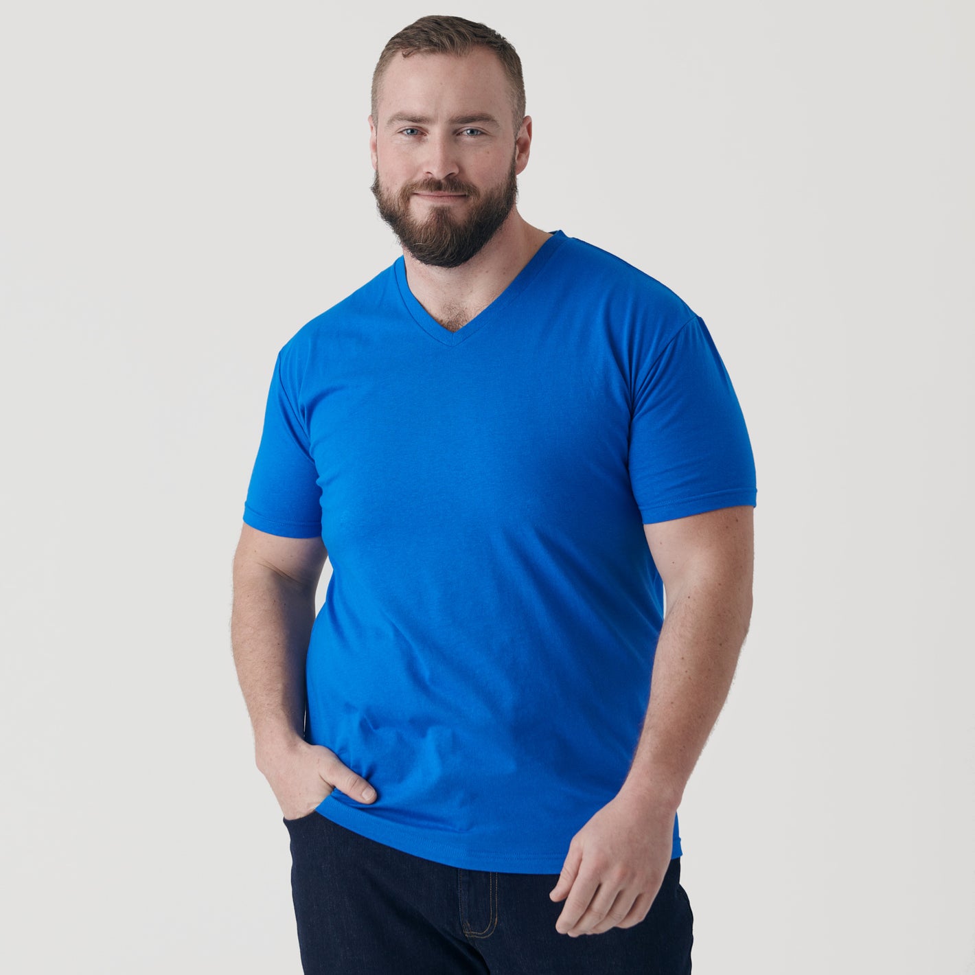 Man wearing Electric Blue V-Neck Tee, hand in pocket, slight smile.