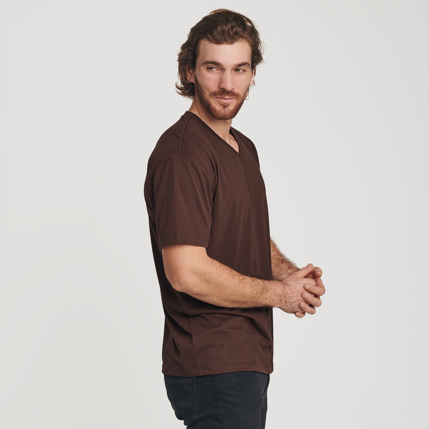 Man wearing Coffee V-Neck Tee, dark pants, slight smile.