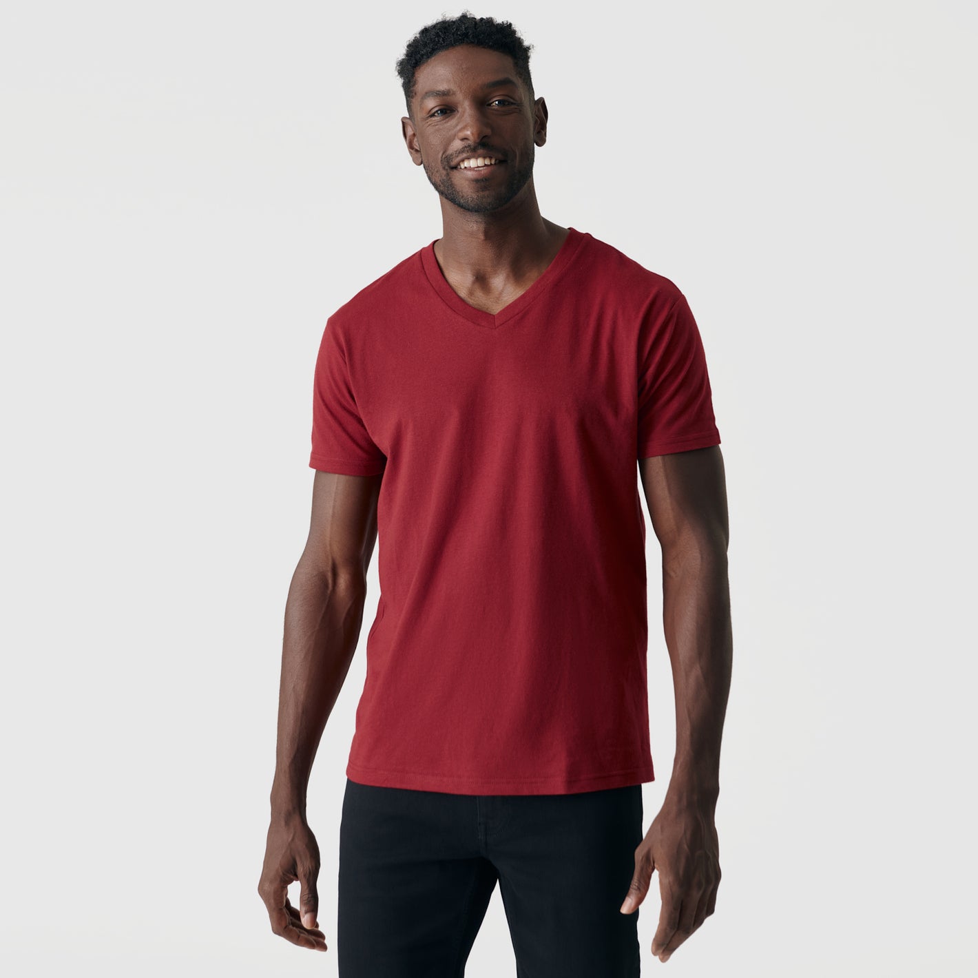 Man wearing Crimson V-Neck Tee and dark pants, smiling slightly.