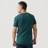 Man wearing Heather Emerald V-Neck Tee, showcasing tattooed arms, looking over shoulder.