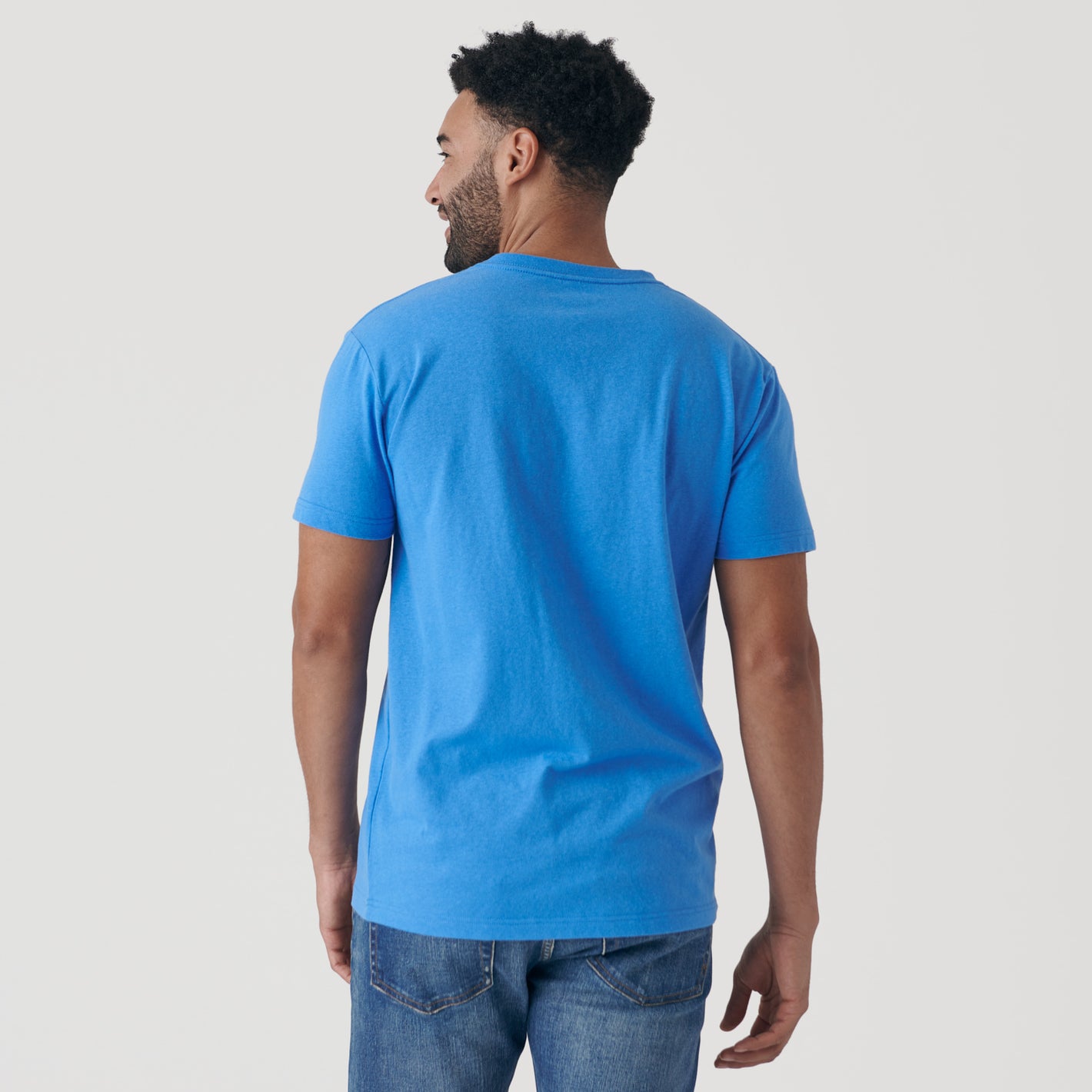 Man wearing Periwinkle Blue V-Neck Tee and blue jeans, back view.