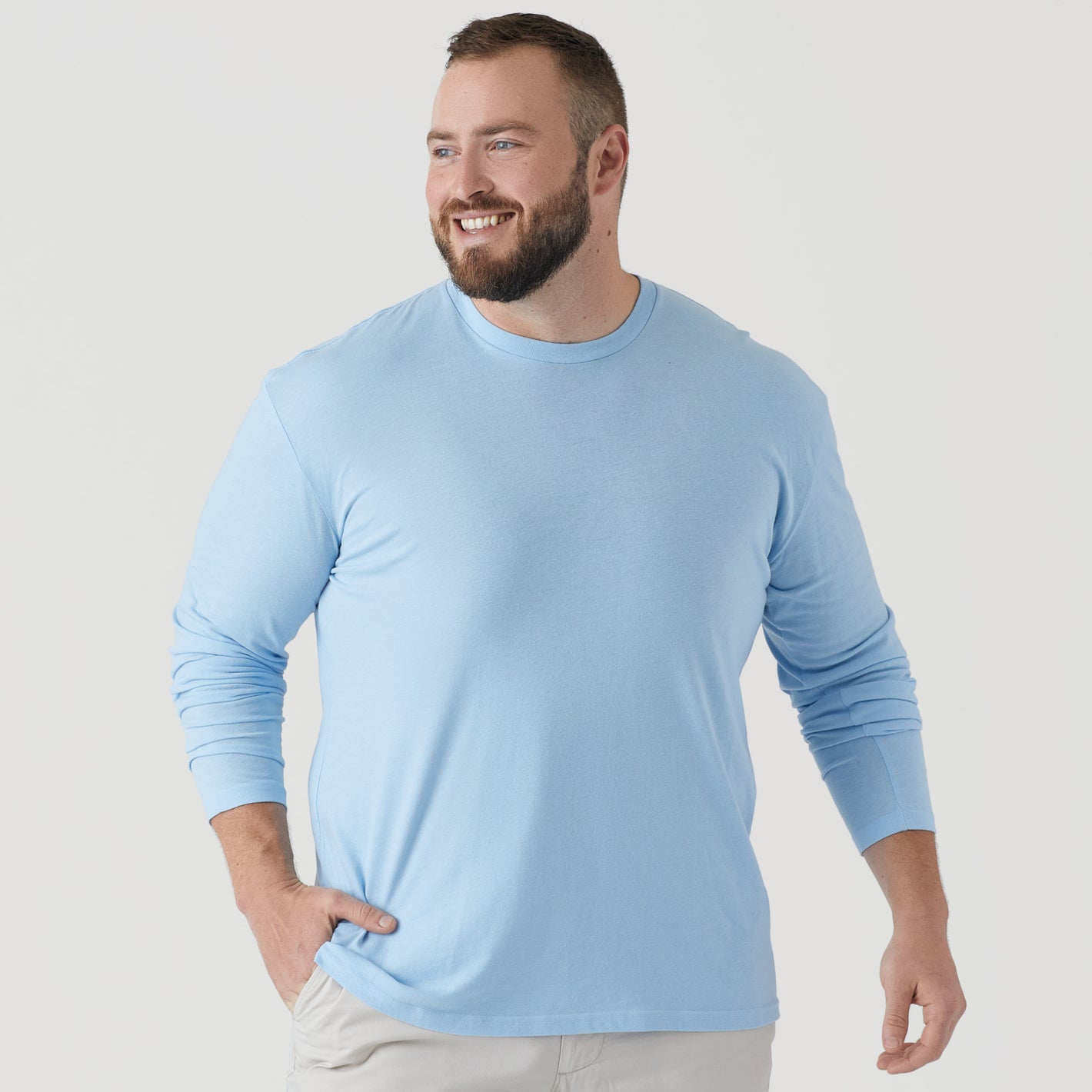 Man wearing Oxford Blue Long Sleeve Crew Neck Tee, smiling, hand in pocket.